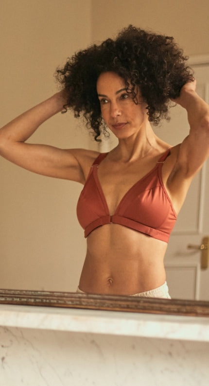 Beautiful, mature woman with a confident look fluffing her hair in the mirror while wearing the velcro front closure bra in terracotta