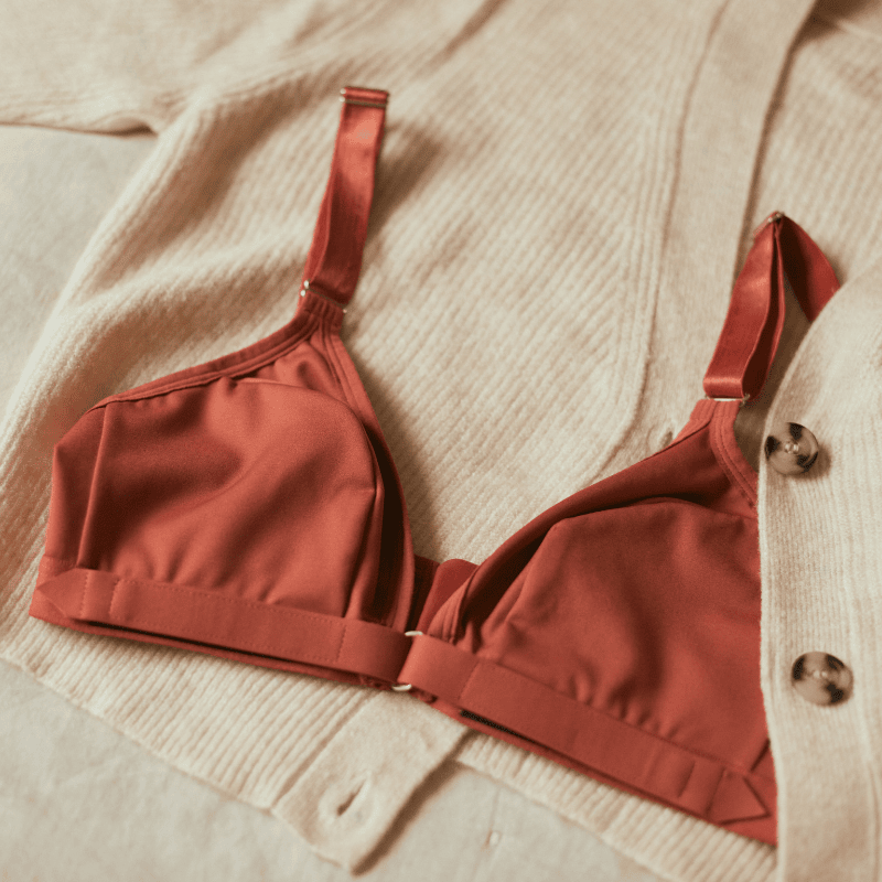 A flatlay of the terracotta-colored Springrose adaptive bra with a velcro front closure, laying on a beige cardigan.
