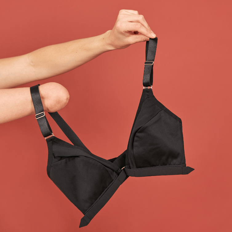 Black adaptive bra from Springrose being held up by two arms, one with a limb difference, against a red background