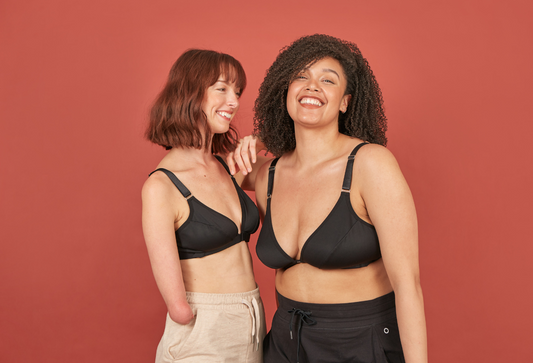 Two beautiful young women laughing and smiling as one leans on the other. Both are wearing Springrose's velcro front closure bra in black.