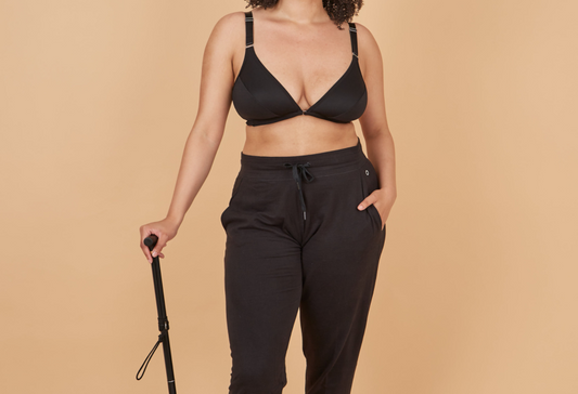 Close up of a young woman using a walking stick, wearing black joggers and the black Springrose adaptive bra