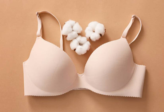 Why the bra was invented: beige molded bra laying on a plain light brown background with cotton close by
