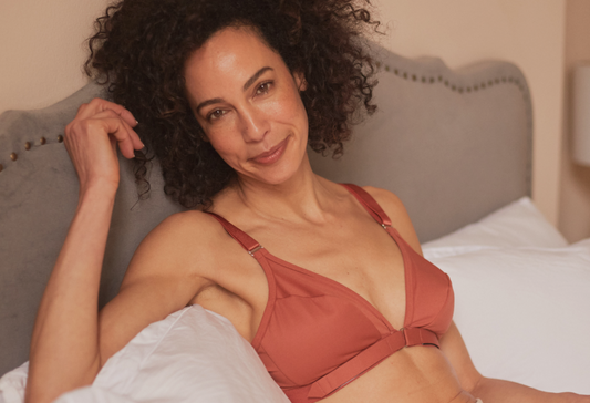 Bra for fibromyalgia: a beautiful mature woman laying in bed, looking at the camera with a half smile, wearing an adaptive bra