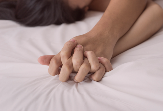 How to make love after shoulder surgery: a couple's intertwined hands on the bedsheets