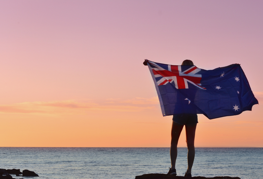 NDIS Low Cost Assistive Technology Guide: person holding the Australian flag on their back as they stare at a sunrise