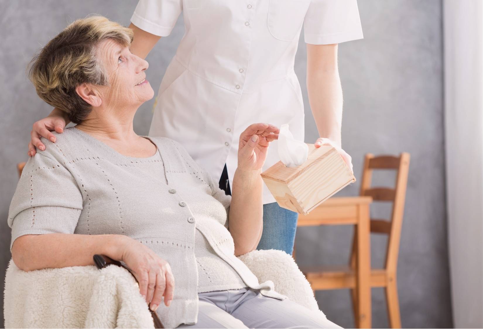 Clothing for assisted living: An elderly woman in a wheelchair being lovingly supported by a caregiver outdoors, showcasing connection and care.