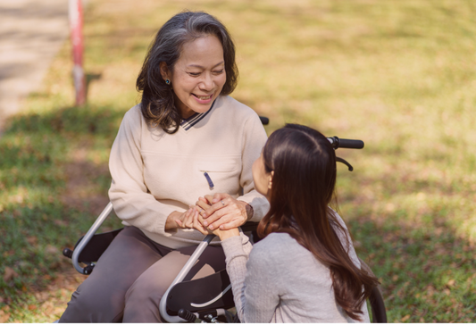 Disability and happiness, mental health strategies. A beautiful mature asian woman in a wheelchair smiling down at her daughter while outside on grass