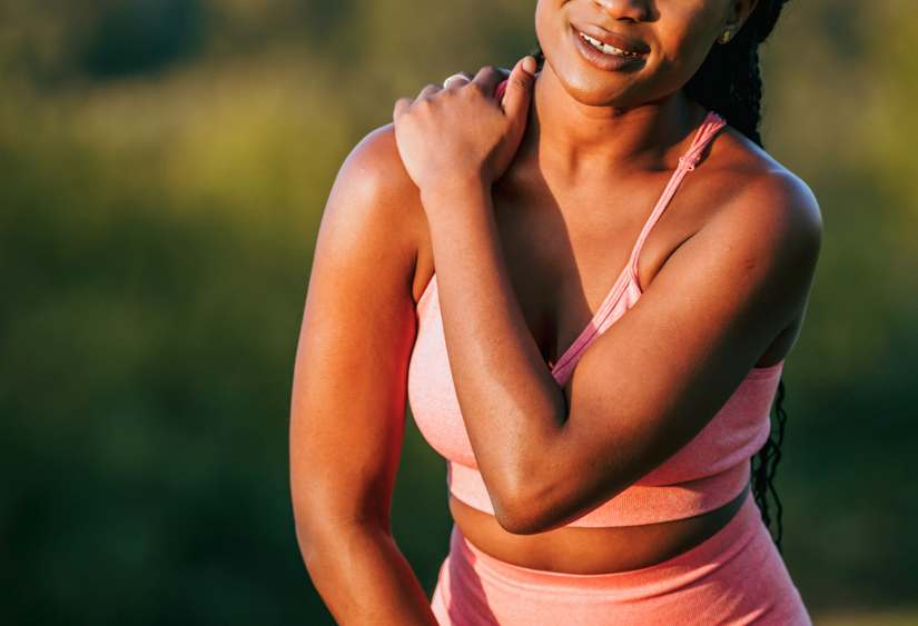 how to put on a bra with a broken shoulder: close up of a woman in a sports outfit holding her shoulder in pain