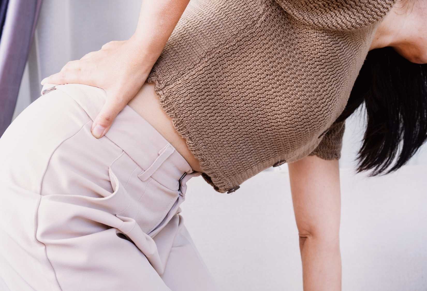Mid back pain from bra: A woman holding her mid back in discomfort.