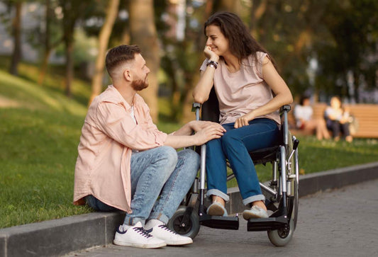 An interabled couple, the woman is in a wheelchair while the man isn't, and they're staring lovingly at each other