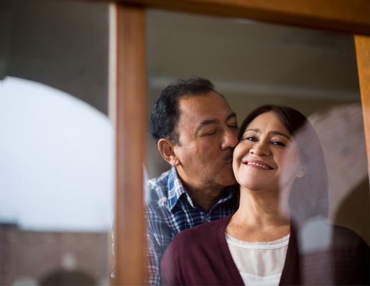 Top relationship tips after surgery: image of a brown man kissing a brown woman on her cheek while she smiles.