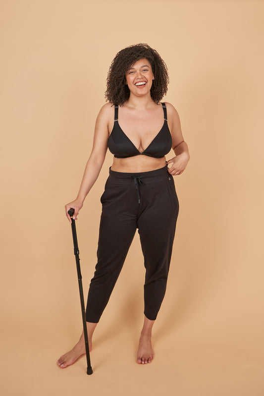 Beautiful woman smiling big at camera while wearing sweatpants and a one handed adaptive bra while leaning on her cane