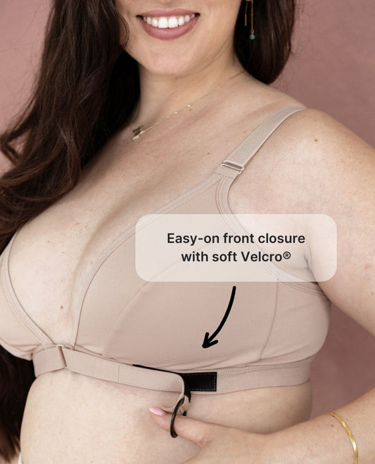 A close up of the Springrose velcro front closure bra. A woman's thumb is hooked through the ring at the end of the velcro strap of the adaptive bra. Text reads: easy-on front closure with soft Velcro.