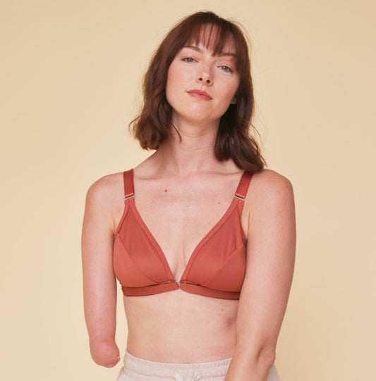One handed young woman with a limb difference staring at camera with a strong, confident expression while wearing the terracotta one arm bra