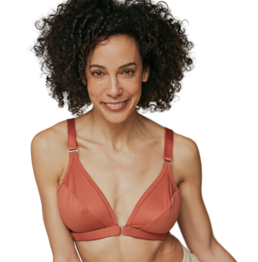 Beautiful, mature woman staring at camera with a soft smile while wearing the best bra for after shoulder surgery in terracotta