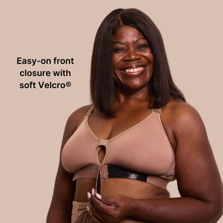 Beautiful mature, black model smiling at the camera while showcasing the Springrose mocha-colored adaptive bra's velcro front closure. Text reads: easy-on front closure with soft Velcro. 