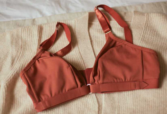 Adaptive front closure bra in terracotta laying on a beige cardigan