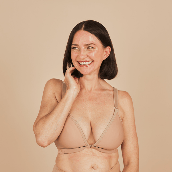 A model smiles while looking off camera while wearing the Springrose velcro bra in beige. 