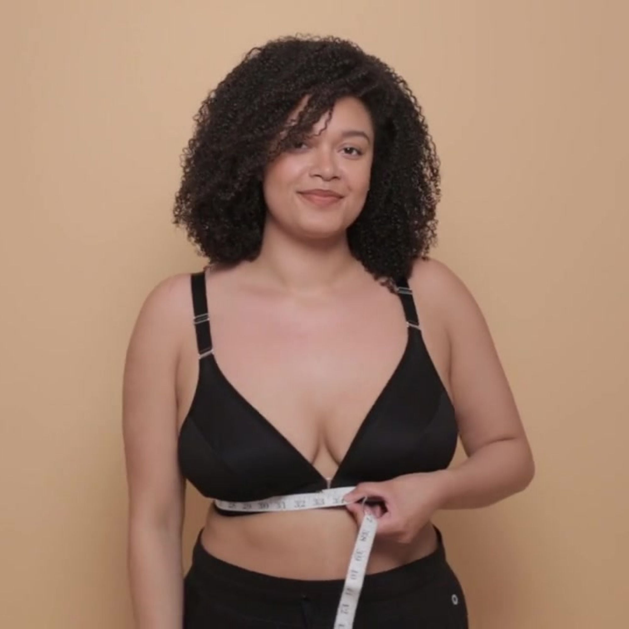 Beautiful young model in the Springrose adaptive bra in black holding a measuring tape around her body and gently smiling at the camera