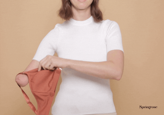 Woman with a limb difference putting on the Springrose one handed bra one handed.