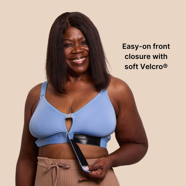 Beautiful mature black model opening the Springrose velcro bra's velcro front closure. The bra is Neptune Blue color. Text reads: easy-on front closure with soft Velcro.